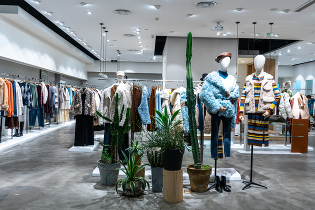 Coats, shirts, and other items hang on clothes racks in a clothing store. 