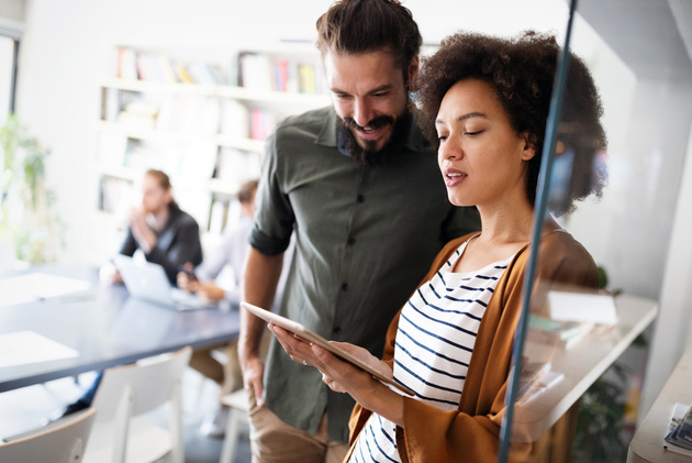A woman and man stand in an office analyzing a chart of data. 